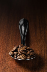 Sticker - Close-up of roasted coffee beans on a spoon, isolated over a wooden surface background