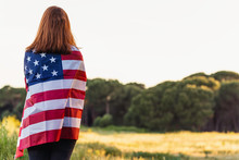 Young Happy Woman From Behind With The United States Flag Enjoying Sunset In Nature. 4th Of July Independence Day Of The United States