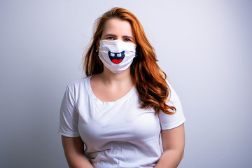 Redhead woman wearing surgical mask with smile design and white shirt.