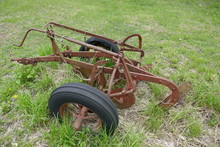 Side View Of Rusty Old Farm Plow Equipment Abandoned In Grassy Field