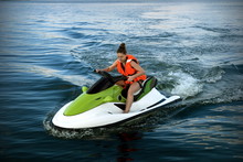 A Young Woman In A Life Jacket Rides A Water Bike On A Lake In Summer.