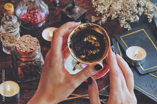 Wiccan witch holding a golden teacup for tea leaf scrying, divination, future reading. Black tea residue in the bottom of a cup, passable for coffee grounds. Witchy vibe with dried herbs and flowers