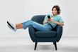 © Syda Productions - people and technology concept - portrait of happy smiling young woman in turquoise shirt and jeans with smartphone sitting in modern armchair over grey background