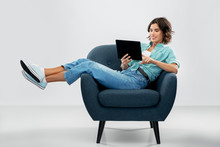 People And Technology Concept - Portrait Of Happy Smiling Young Woman With Tablet Pc Computer Sitting In Modern Armchair Over Grey Background