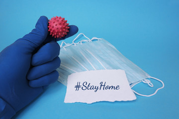 Hashtag steyhome, medical mask and hand holding coronavirus covid-19 on a blue background.