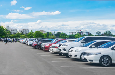 Wall Mural - Car parking in large asphalt parking lot with trees, white cloud and blue sky background.