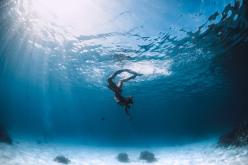 Wall Mural - Freediver girl in bikini with fins glides underwater in blue transparent sea