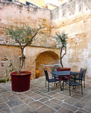 The Ancient City Of Matera, Carved Into The Rock. Old Stone Blocks And Streets Of The City. In 2019-the Cultural Capital Of Europe. Beautiful View Of Interior Courtyard With Chairs And Table. Italy.