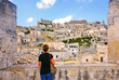 young woman look at panorama of town Matera (Sassi di Matera), European Capital of Culture 2019,and UNESCO Heritage  site  with blue sky and clouds, Basilicata, southern Italy          