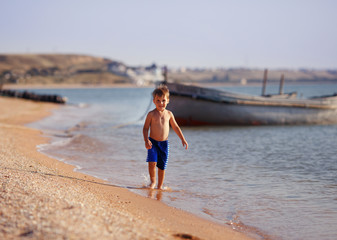 a boy runs on the beach near a boat