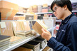 © zephyr_p - Asian man customer choosing new paper notebook from display rack in stationery shop. Buying office supply concept