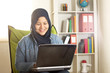 © airdone - Portrait of happy smiling Asian muslim woman working with laptop in her bedroom, casual modern lifestyle