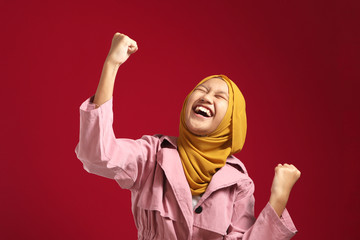 Wall Mural - Portrait of happy success confident young teenage Asian muslim girl shows winning gesture celebrating victory, wearing yellow hijab