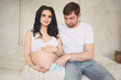 © Алина Троева - Pregnancy and people concept - happy man hugging his beautiful pregnant wife at home. Future parents waiting unborn baby. Love, relationship, birth, happy family concept - young lovely married couple