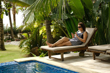 Portrait Of The Woman, In The Striped Dress And Barefoot, Using Smartphone On The Wooden Sun Bed Near The Pool. Vacation