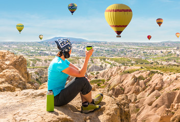 Wall Mural - Woman drinking tea and looking at hot air balloons, Cappadocia, Turkey. Concept of travel, meditation, relaxation