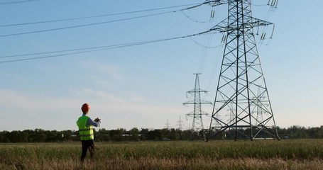 Wall Mural - an engineer in uniform enters the frame and inspects the power lines using a tablet, sunset backgrou
