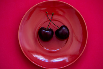 Two wild cherries or gean berries on a red plate