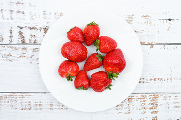 Wall Mural - red strawberries on a white plate stand on a wooden white table