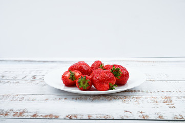 Sticker - red strawberries on a white plate stand on a wooden white table