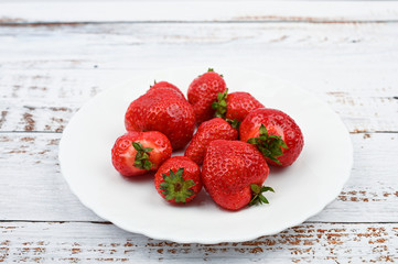 Sticker - red strawberries on a white plate stand on a wooden white table