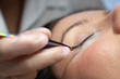 © Михаил Решетников - Woman lies on eyelash extension procedure in a beauty salon. Lashmaker holds tweezers with a bunch of artificial eyelashes. Close-up of a craftsman in gloves.