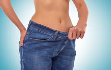 Slender Girl In Big Jeans On A Blue Background. Losing Weight.