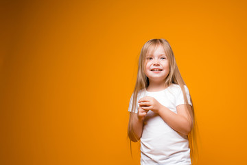 Portrait of a modest long-haired girl child holding hands near the chest and smiling on an orange background