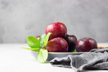 Wall Mural - Purple plums with leaves and knife on ceramic plate, light grey concrete background.