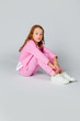© Julie Boro - girl in a pink tracksuit and sneakers sits on a light gray background