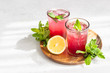 Cold sparkling hibiscus or karkade tea with lemon, mint and ice in glasses on a grey stone background. Summer drink, lemonade.