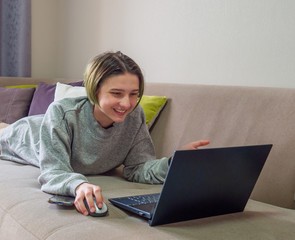 Happy teenage girl blogger working online on laptop with smartphone on sofa at home. Concept of distance education or learning, online shopping, communication with friends