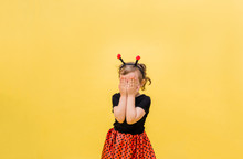 Portrait Of A Little Girl In A Ladybug Costume Closed Her Eyes On A Yellow Isolated Background With Space For Text.