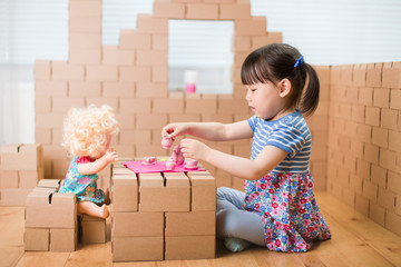 Wall Mural - toddler girl pretend play baby care in a cardboard block house