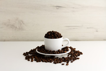 A little cup is full of coffee beans on a light background