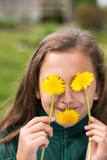 Fototapeta  - Little Girl With Dandelions In Hands Near Eyes And In Mouth In Garden Close-Up.