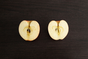 Closeup to a fresh red apple cutting in two pieces with apple seeds over a dark brown wooden table