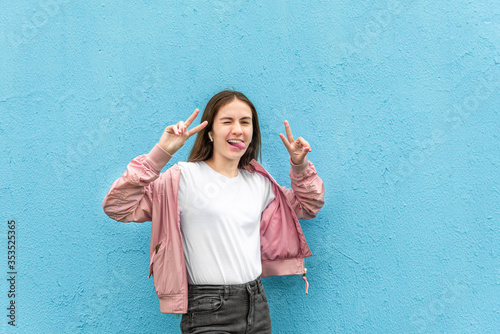 Cuadros en Lienzo Portrait of funny caucasian teen girl in blank white t-shirt and pastel pink bomber jacket against blue city wall solid background