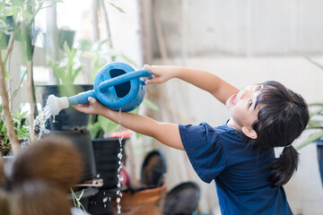 Asian kid girl 6 years old watering water the plant in the garden outside.Stay home plant growing learning activity and child responsibility.Happy asian girl watering garden in morning.Home school.