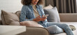 © insta_photos - Smiling afro american millennial woman user holding smart phone watching video, playing game, shopping, chatting in mobile technology application sitting on sofa at home. Close up view, banner design.