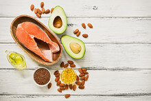 Food high in omega-3 fatty acids on a white wooden background. Healthy eating concept. Salmon, avocado, flax seeds, fish fat capsules, oil, almonds. Top view, flat lay.