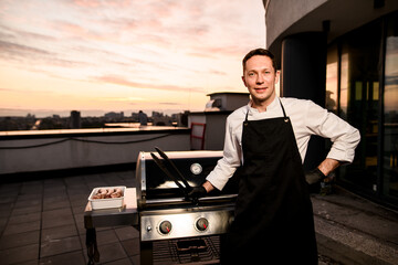 professional male chef holds tongs in his hand and standing near barbecue equipment.