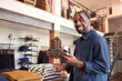 Portrait Of Male Owner Of Fashion Store Using Digital Tablet To Check Stock In Clothing Store