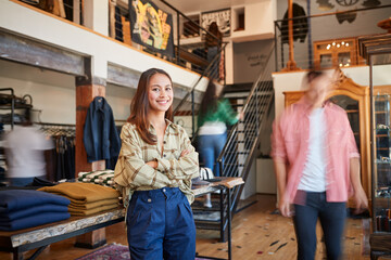 Wall Mural - Portrait Of Female Owner Of Fashion Store Standing In Front Of Clothing Display With Customers