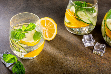 Summer healthy lemonade, cocktails of citrus infused water or mojitos, with lime lemon orange, ice and mint, diet detox beverages, in glasses on gray background.