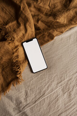 Wall Mural - Blank screen smart phone on ginger blanket. Flat lay, top view. Copy space mockup template.