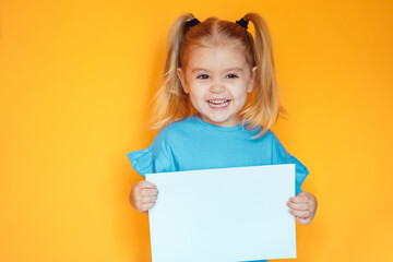  Cute little girl holding a smartphone and looking surprised with her mouth open, on an orange background