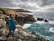 A Woman And Her Dog Stand On Rugged Cliffs At Hushinish On The Isle Of Harris