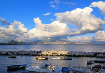 Wall Mural - Sea port of city of Naples with people, small fishing boats on water with colorful sun reflections and Vesuvius in background, Napoli Italy