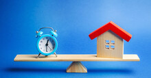 A Clock And A Miniature House On The Scales. Mortgage And Loan Concept. Real Estate And Risks. Property Insurance. Credit. Tax Payment. Utilities. Construction Investment